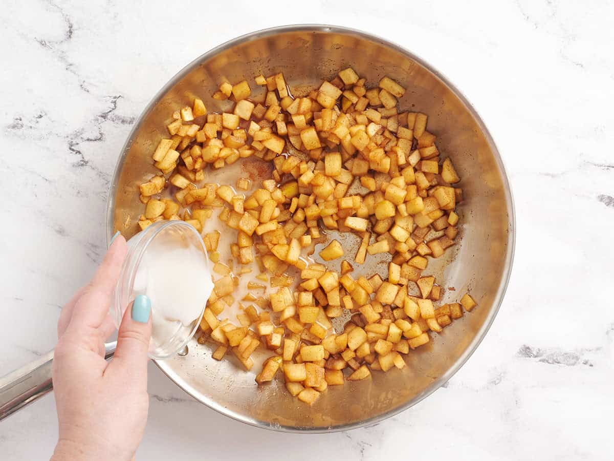 Une suspension de fécule de maïs versée dans une poêle avec une pomme en dés ramolli.