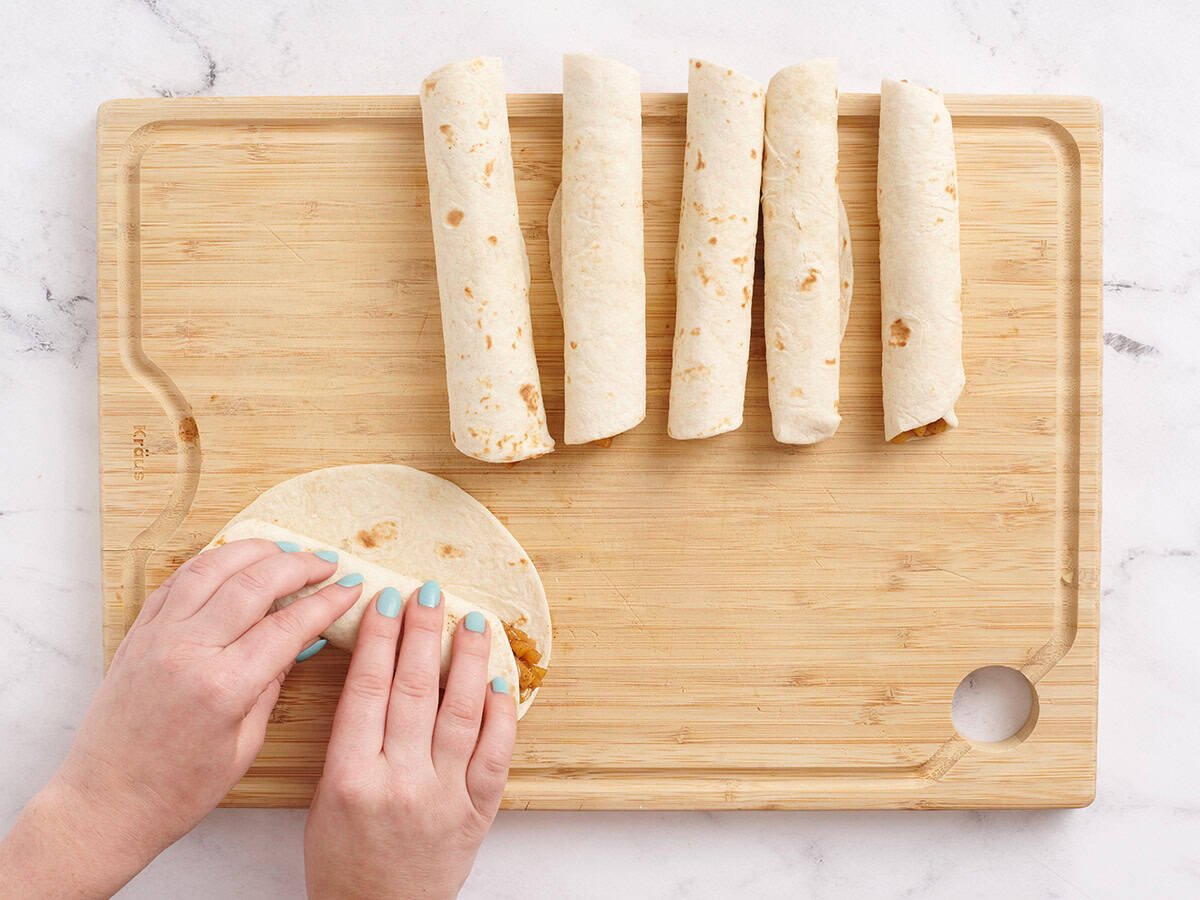 Les mains enroulant une tortilla de farine pour faire une pomme à la farine maison.