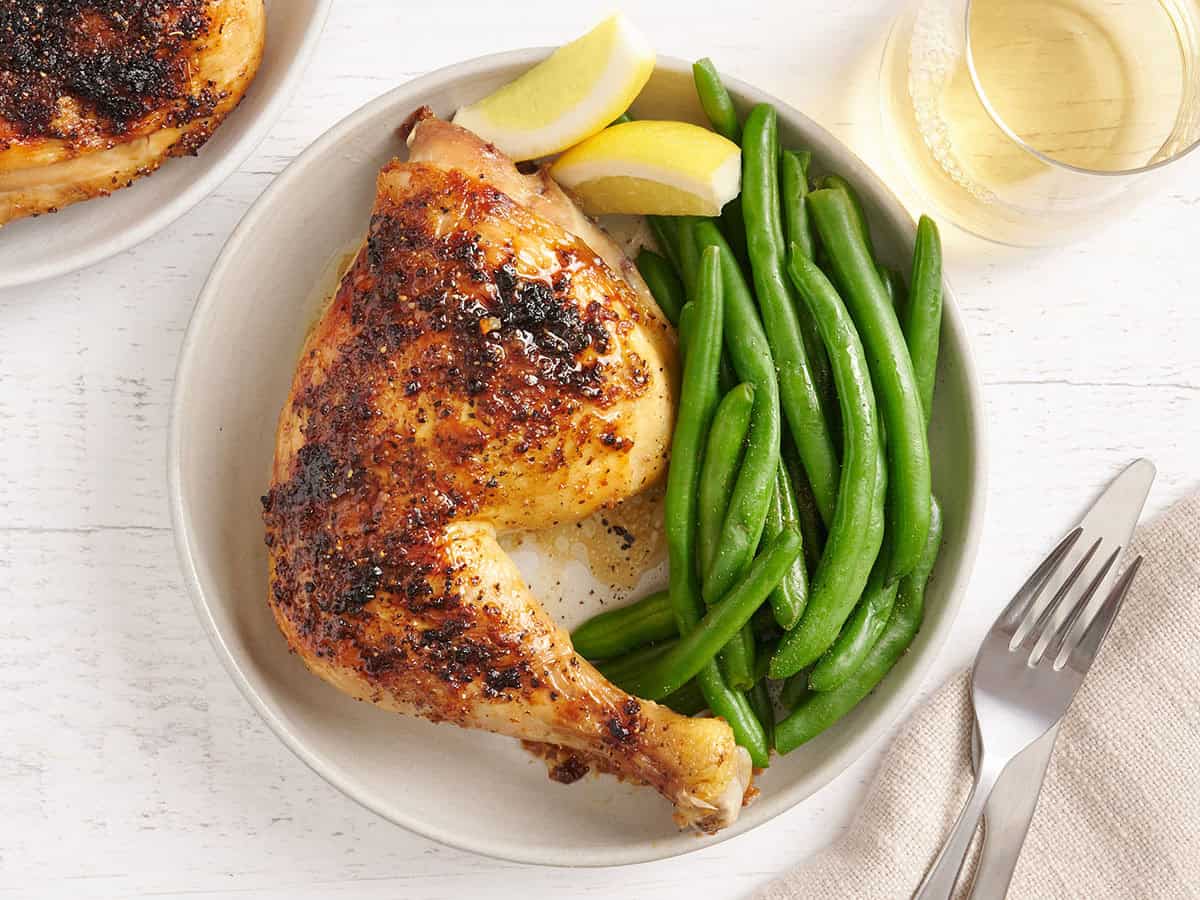 Vue aérienne d'une cuisse de poulet cuite au four sur une assiette avec des haricots verts et des quartiers de citron.