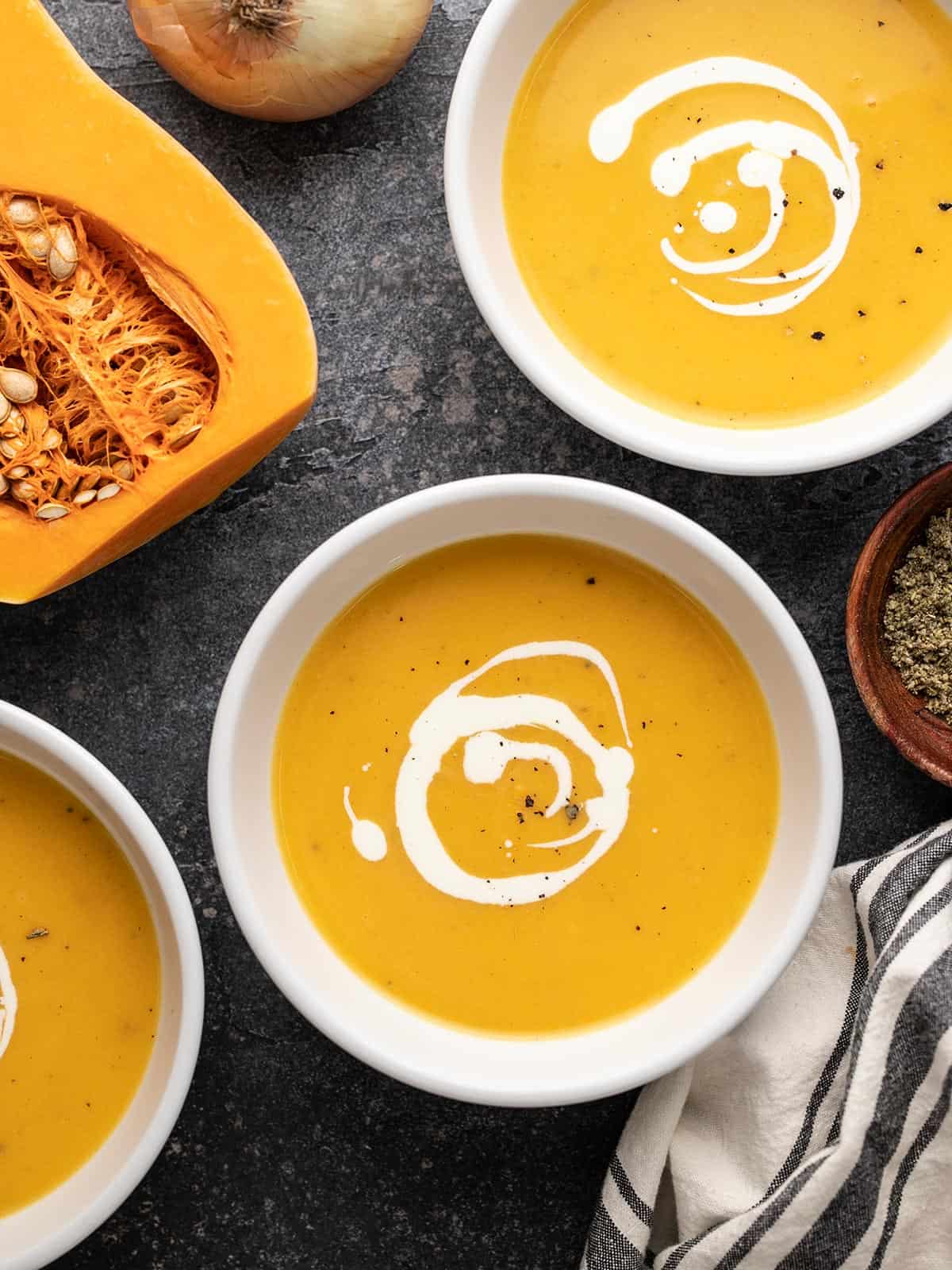 Trois bols de soupe de courge musquée à côté d'une courge coupée en deux.