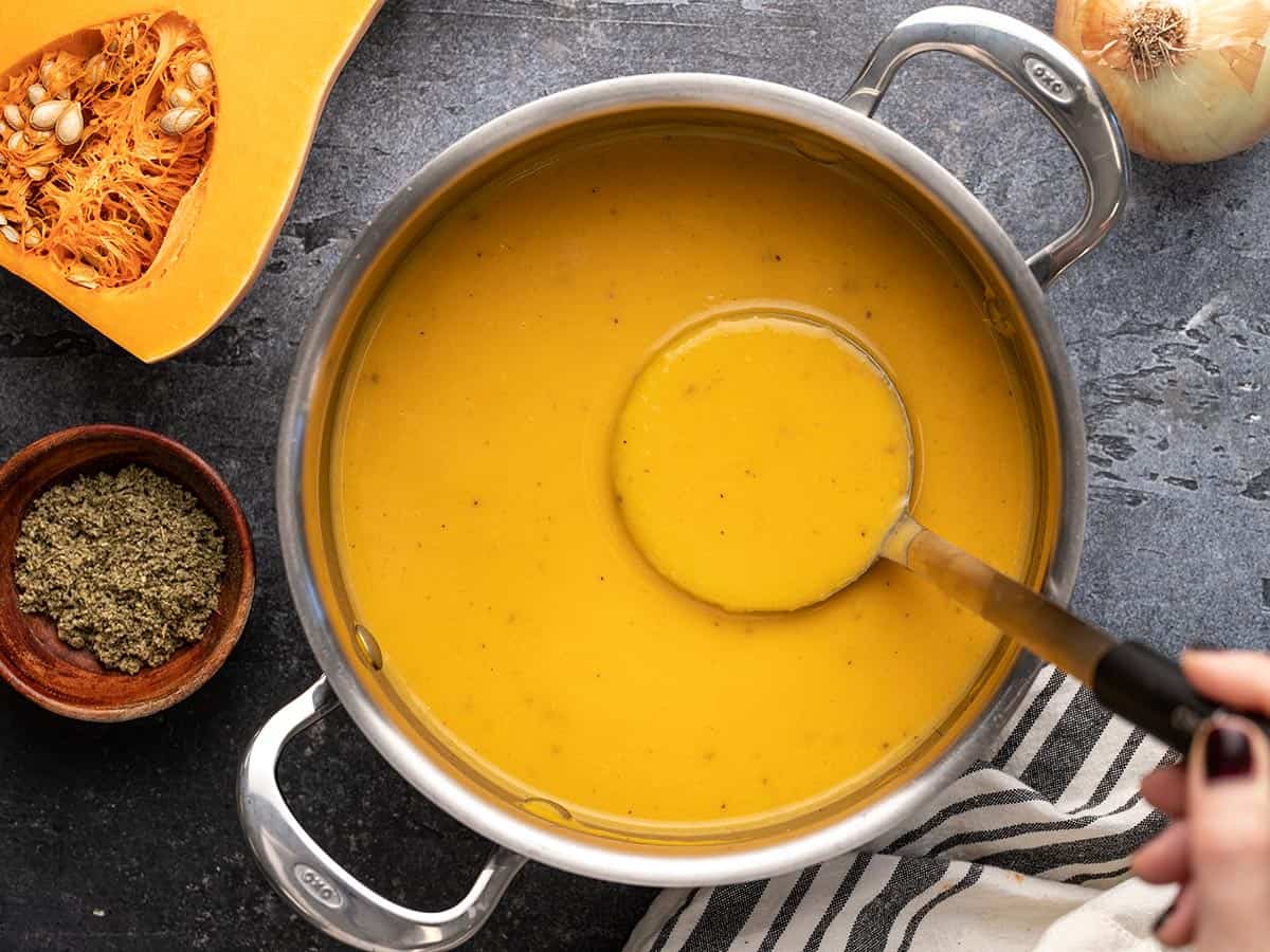Vue aérienne d'un pot rempli de soupe de courge musquée avec la louche levée. 