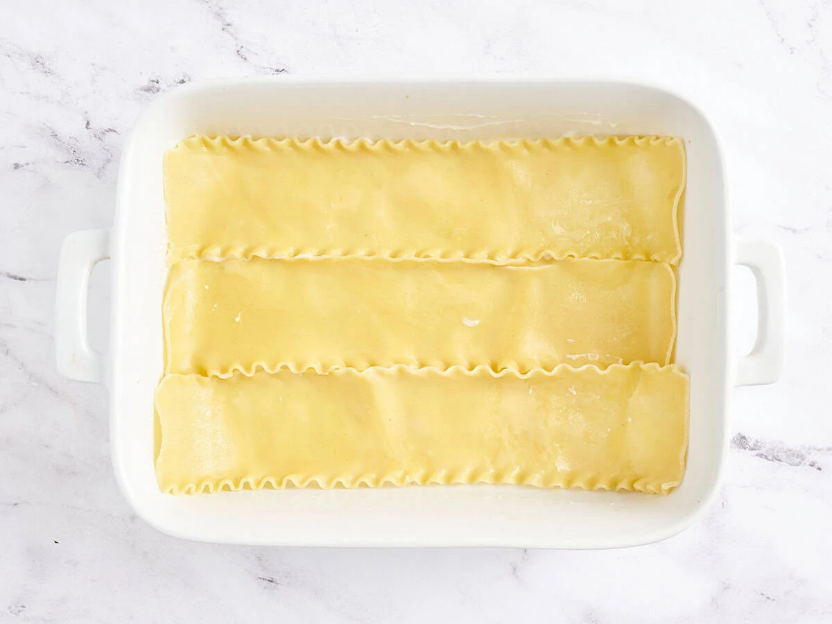 Nouilles de lasagne cuites ajoutées à un plat allant au four.