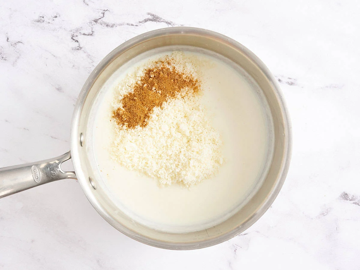 Parmesan et assaisonnements dans une sauce à la crème blanche dans une casserole.