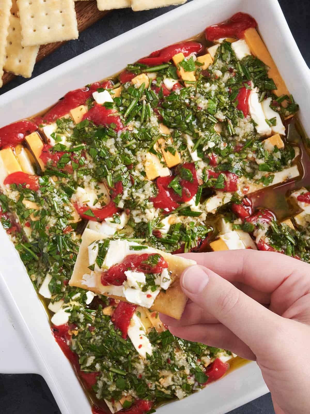 Vue aérienne d'une poêle de fromage mariné, avec une main tenant un cracker avec du fromage.