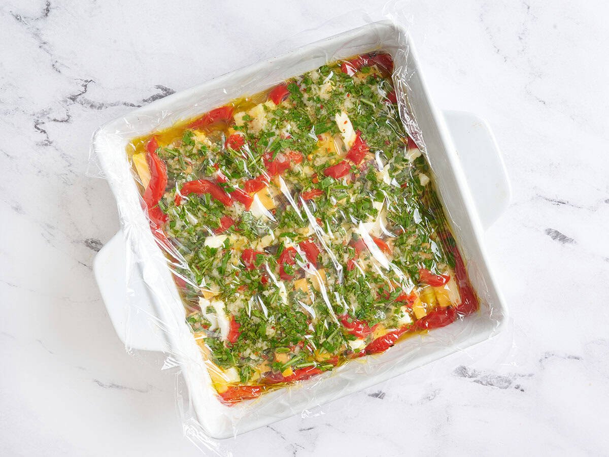 Un plat allant au four de fromage mariné recouvert d'une pellicule plastique.