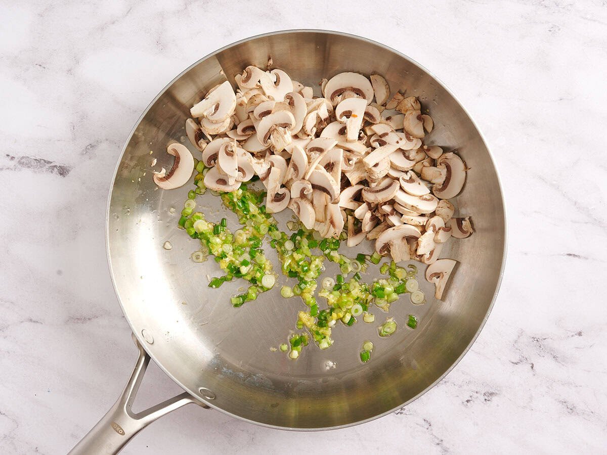 Champignons dans une poêle avec oignons verts sautés.