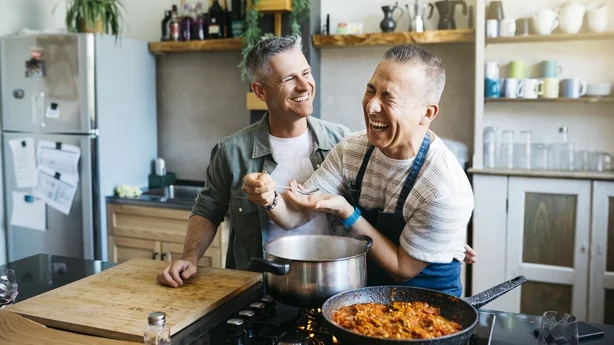 Couple gay joyeux d'âge moyen parlant et s'amusant tout en cuisinant dans une cuisine