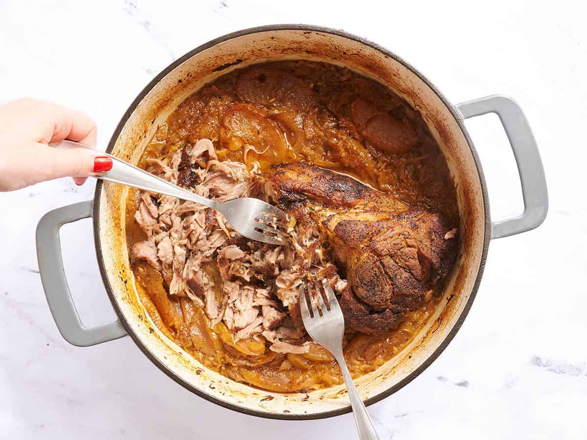 Fourchettes déchiquetant un mégot de porc dans une cocotte.