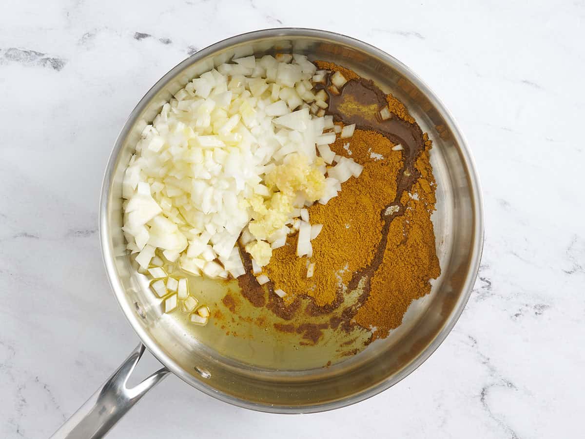 Épices, oignons coupés en dés, ail et gingembre dans une poêle.