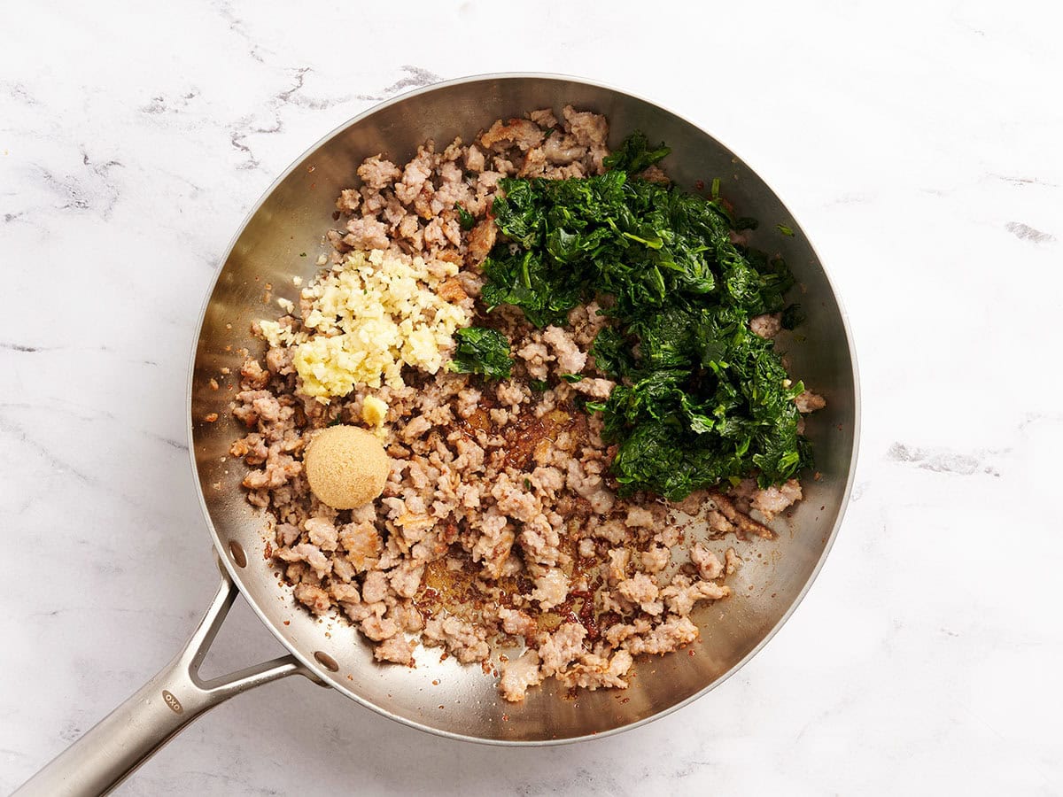 Porc haché doré, épinards, sucre et aromates dans une poêle.