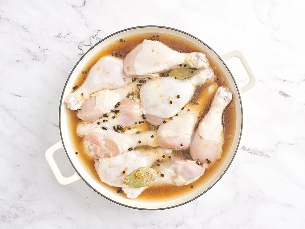 De l'eau ajoutée dans une casserole avec des pilons de poulet et une marinade.