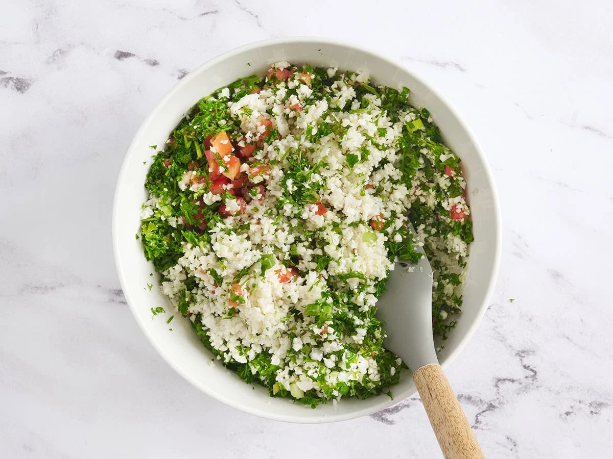 Une spatule pliant un taboulé de chou-fleur dans un bol.