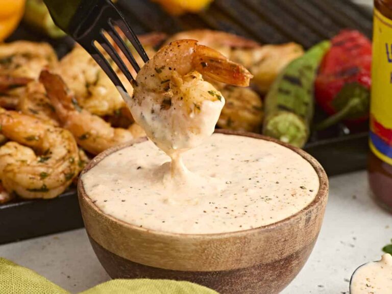 Side view of a shrimp being dipped into remoulade sauce