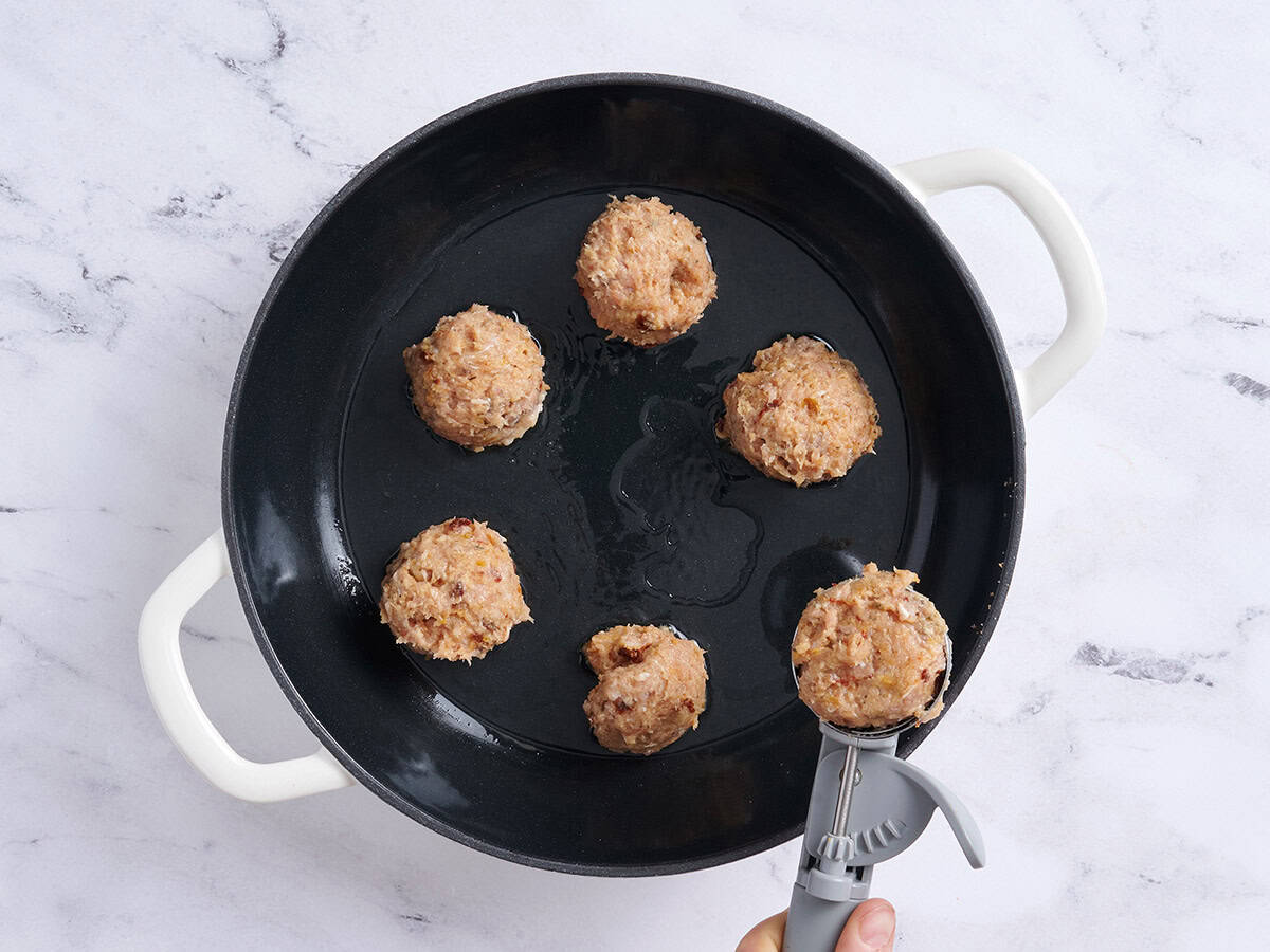 Une cuillère à glace ajoutant des boulettes de viande dans une poêle.