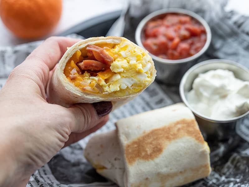 Une main tenant la moitié d'un burrito pour le petit-déjeuner, le côté ouvert faisant face à la caméra.