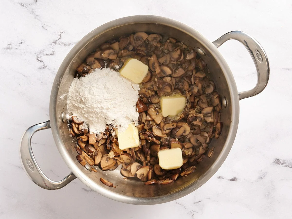 Beurre et farine ajoutés à une poêle de champignons sautés.