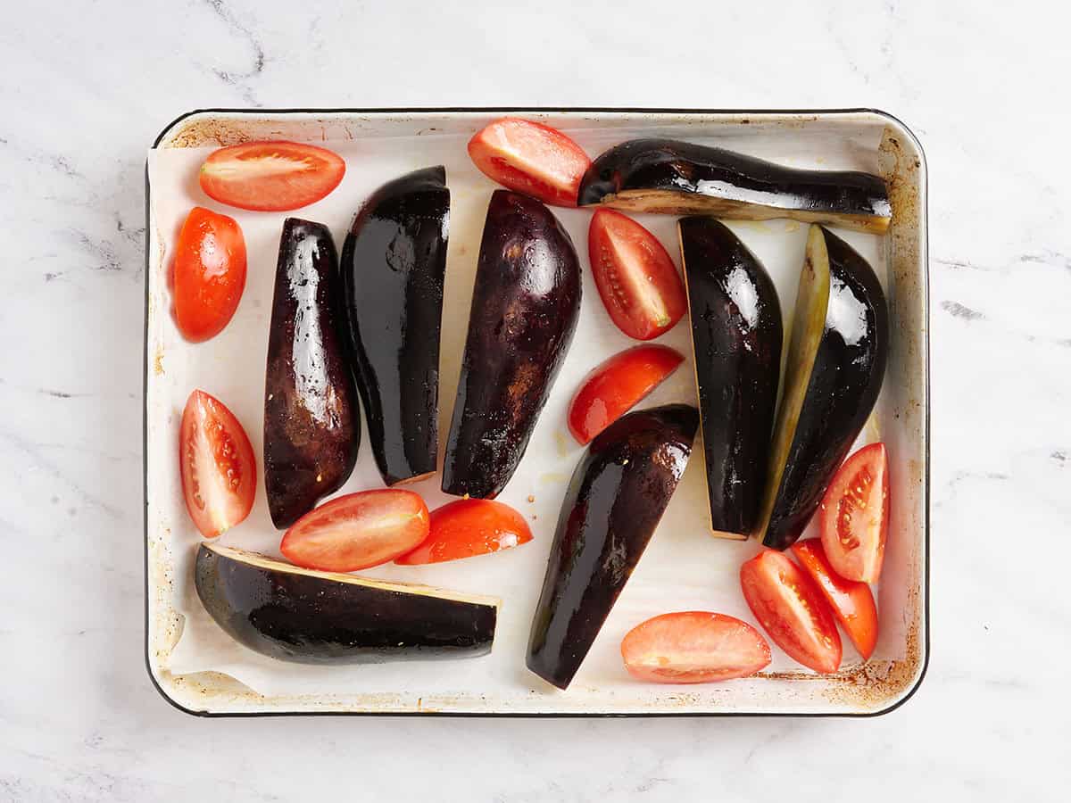 Quartiers d'aubergines et de tomates rôtis sur une plaque à pâtisserie.