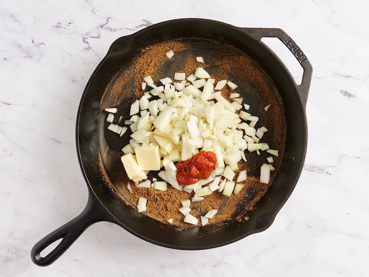 Oignon coupé en dés dans une poêle avec la pâte de curry rouge.