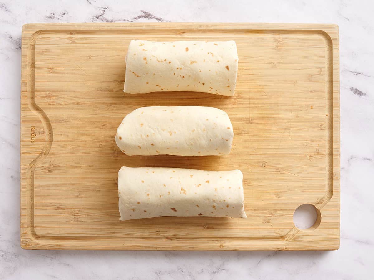 Trois roulés de thon roulés sur une planche à découper en bois.