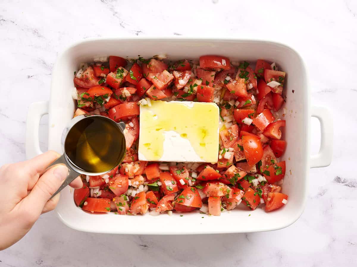 Un filet d'huile d'olive à la main sur les tomates, les oignons et le fromage feta.