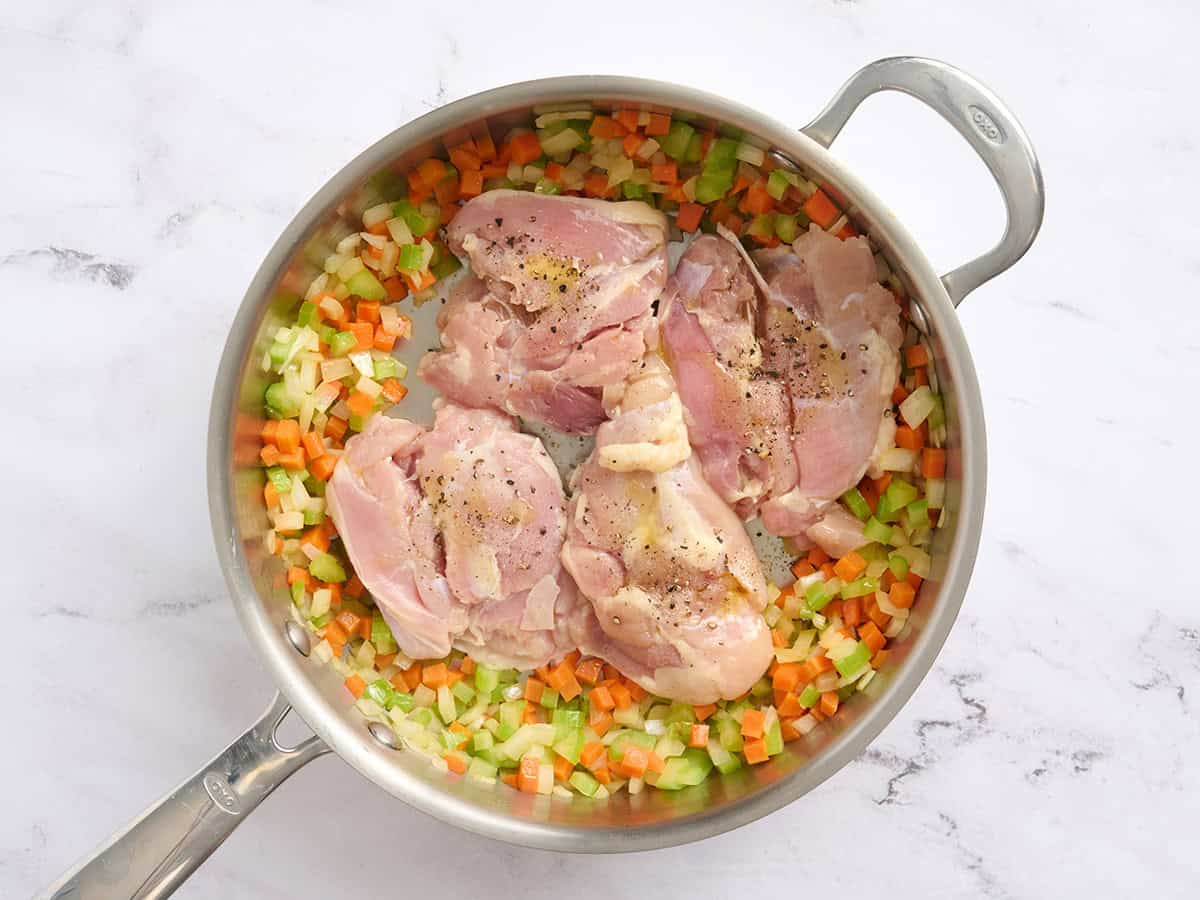 Cuisses de poulet ajoutées à une poêle avec des carottes, des oignons et du céleri sautés.