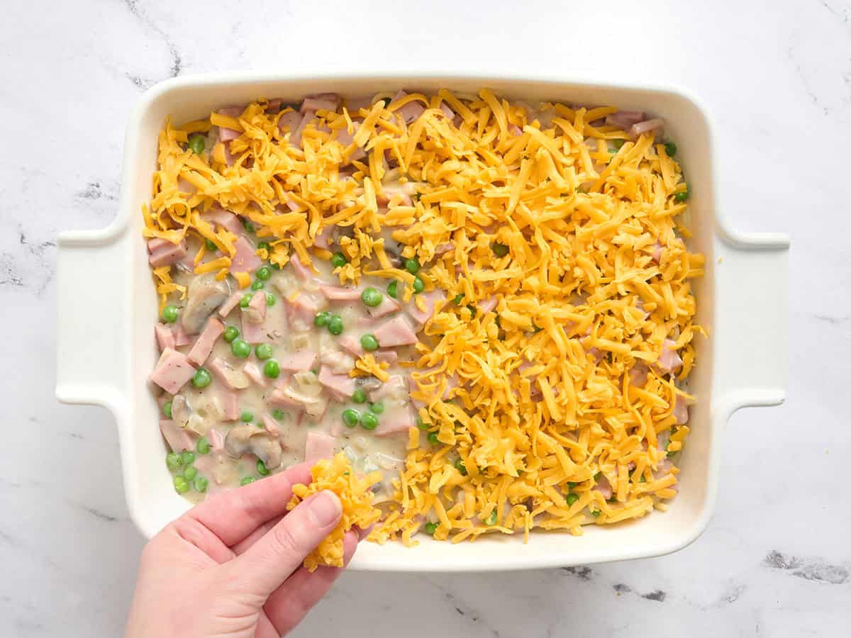 Une main saupoudrée de cheddar sur un tetrazzini au jambon.