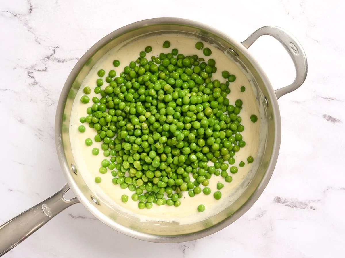 Petits pois ajoutés à une sauce à la crème dans une poêle.