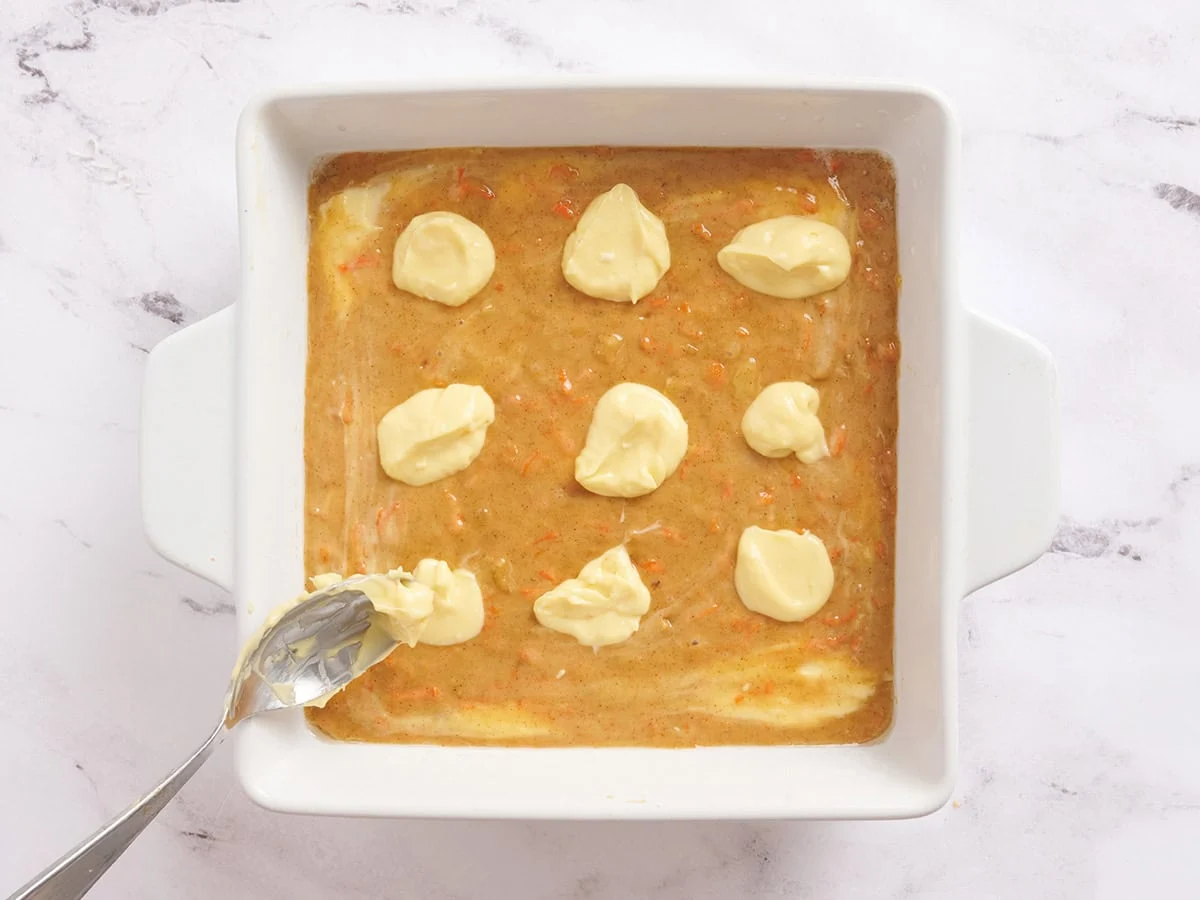 Cuillerées de gâteau au fromage ajoutées à la pâte pour les barres de gâteau aux carottes.