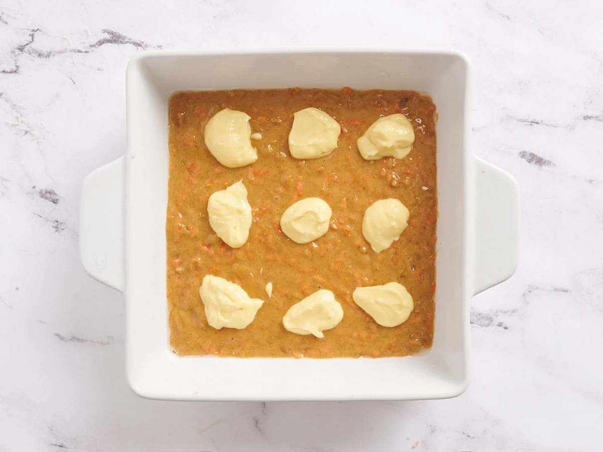 Une couche de mélange à gâteau aux carottes ajoutée à un plat allant au four avec le mélange à gâteau au fromage déposé sur le dessus.