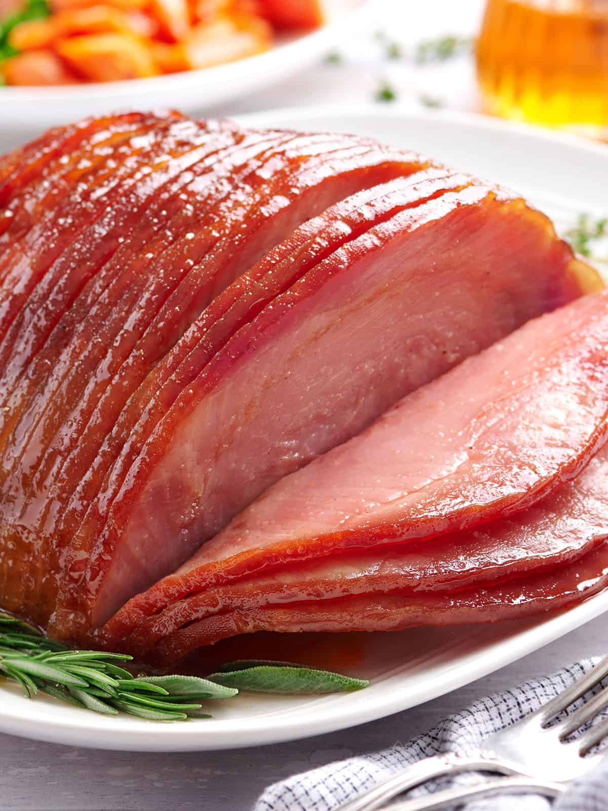 Vue latérale de tranches de jambon glacé au miel sur une assiette aux herbes.