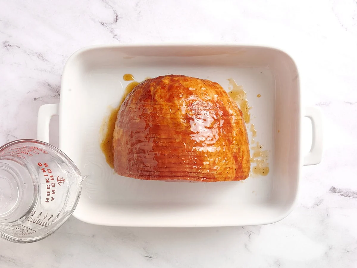 De l'eau est versée dans un plat allant au four avec du jambon glacé au miel.