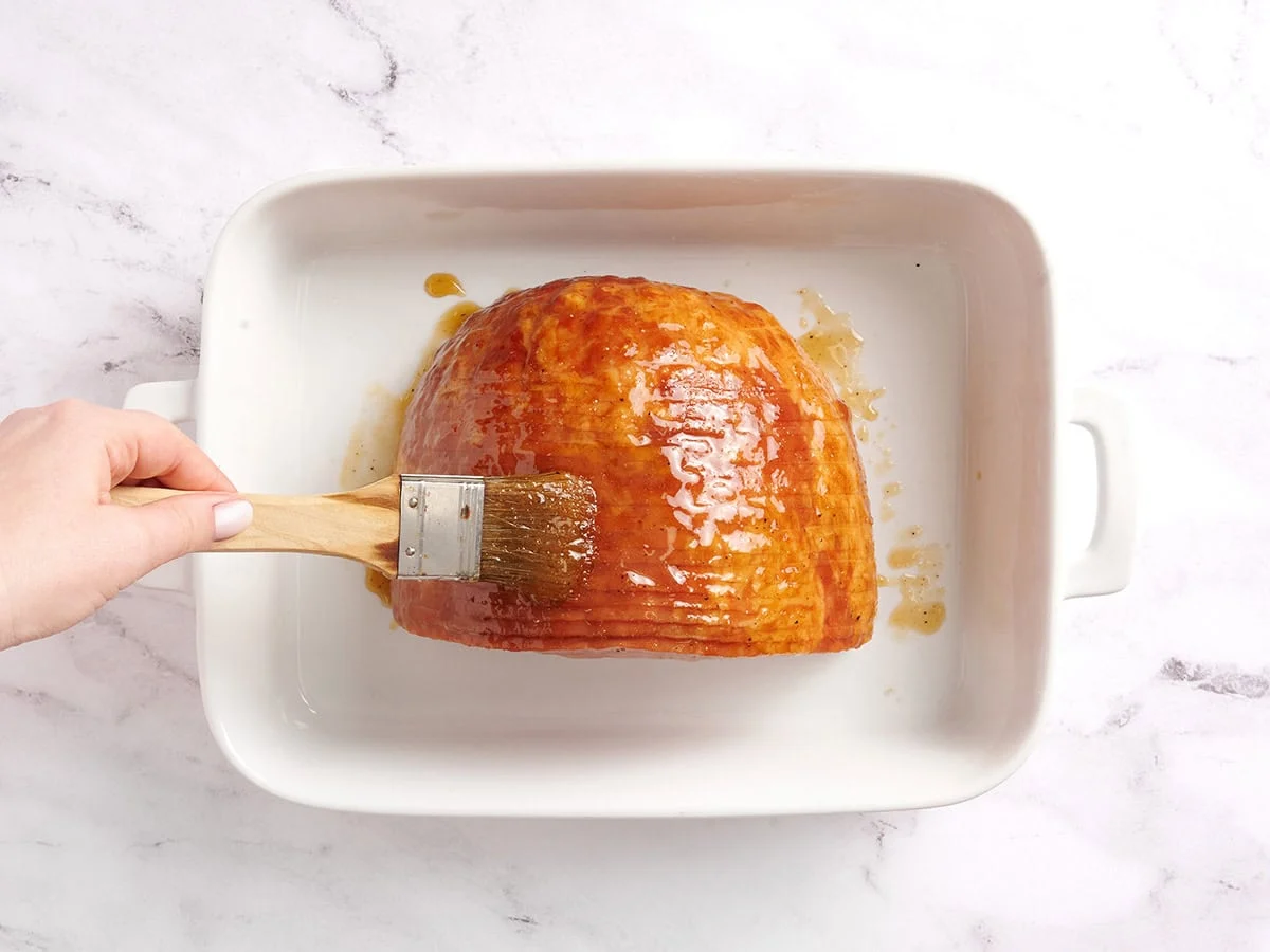Un pinceau pour ajouter du glaçage au miel sur un jambon coupé en spirale.