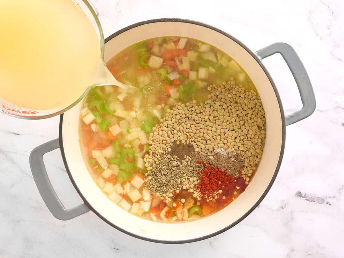 Lentilles séchées, assaisonnements et bouillon ajoutés à une casserole avec des légumes.