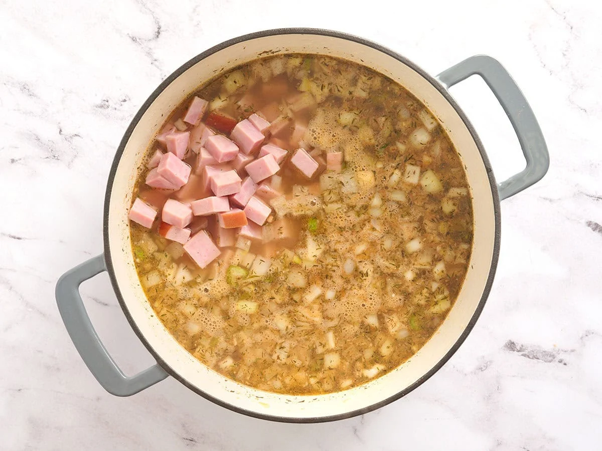 Dés de jambon ajoutés à une marmite de bouillon et de légumes.