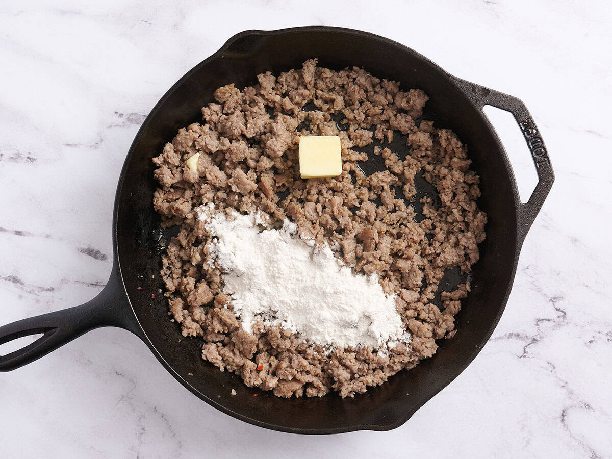 Farine et beurre ajoutés à la chair de saucisse dorée dans une poêle.
