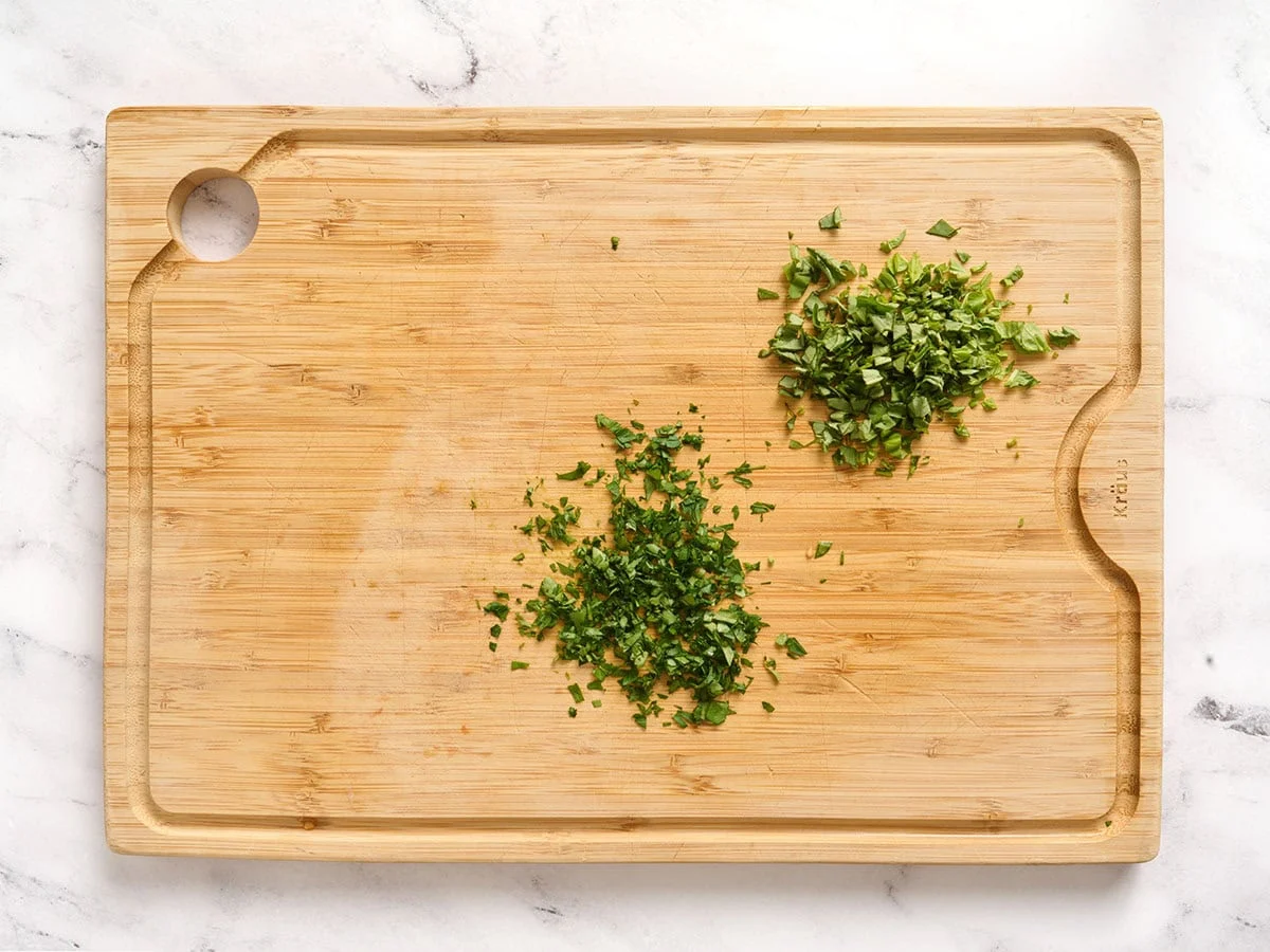 Persil haché et basilic sur une planche à découper en bois.