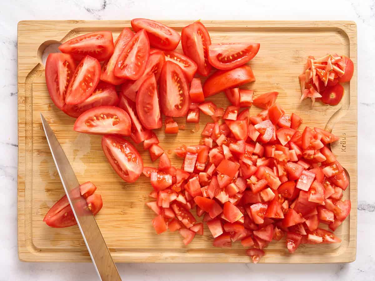 Un couteau coupant des tomates roma sur une planche à découper en bois.