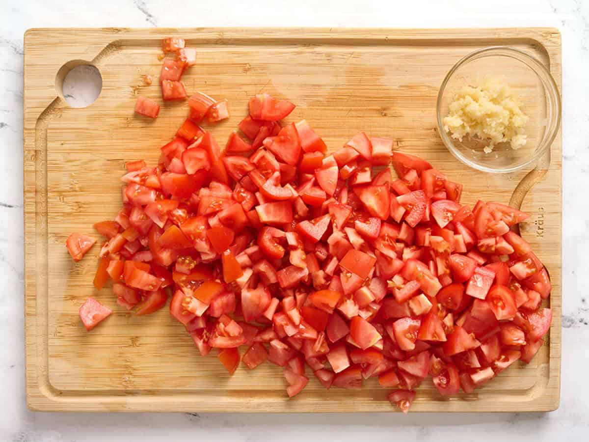 Tomates roma coupées en dés et ail émincé sur une planche à découper.