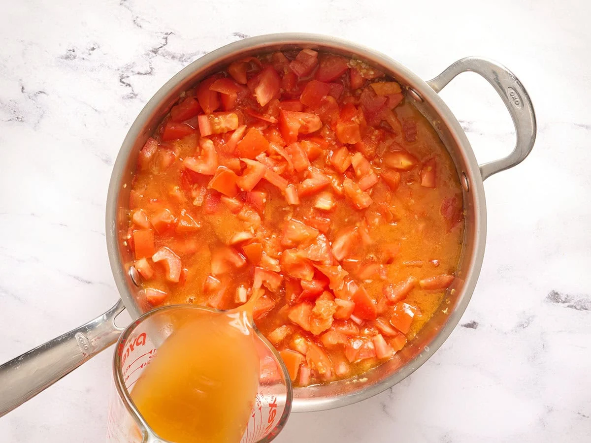 Bouillon ajouté aux tomates dans une poêle.