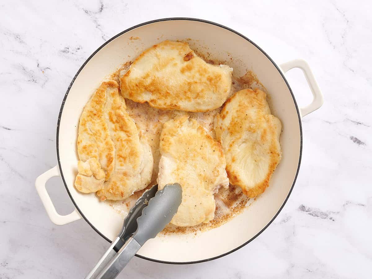 Pinces de cuisine retournant les poitrines de poulet dans une poêle.