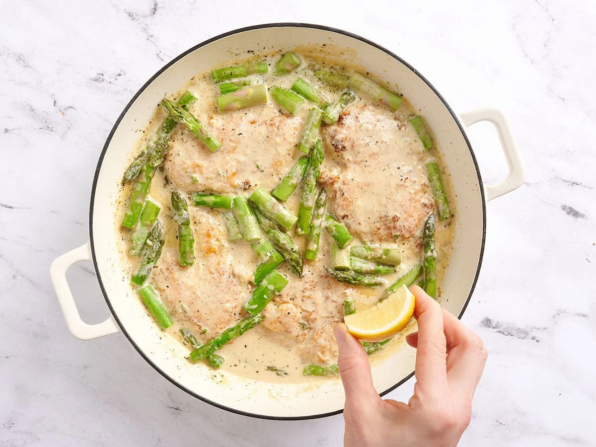 Presser à la main un citron sur un poulet aux asperges crémeux dans une poêle.