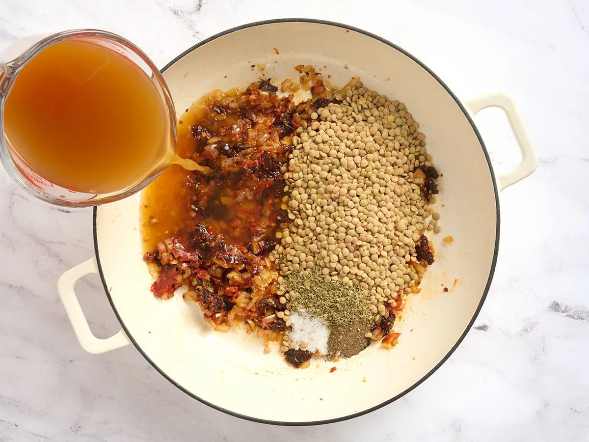 Bouillon et lentilles séchées ajoutées à une casserole avec des tomates séchées.