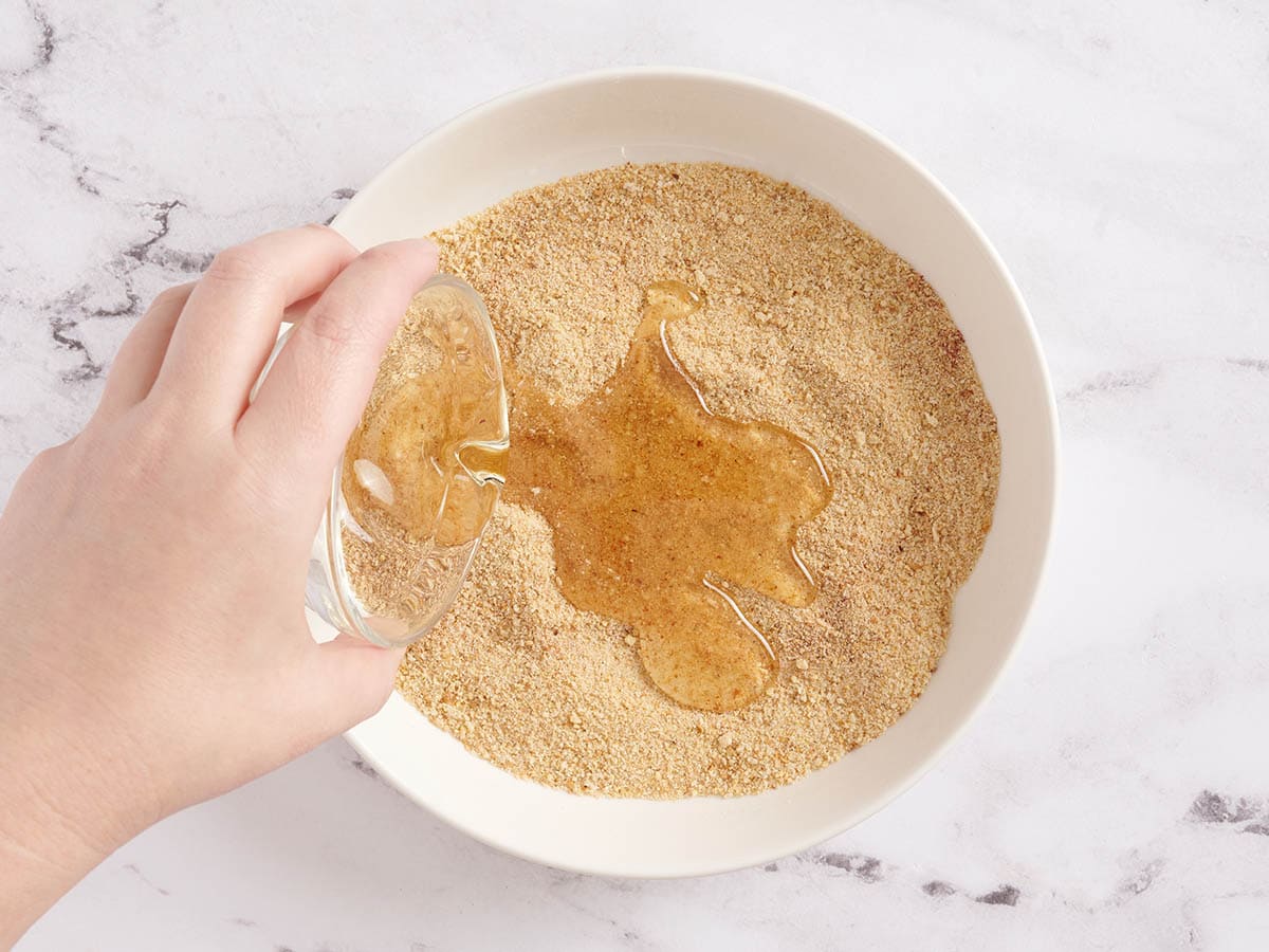 Une main versant de l'huile dans un mélange de chapelure pour les nuggets de poulet.