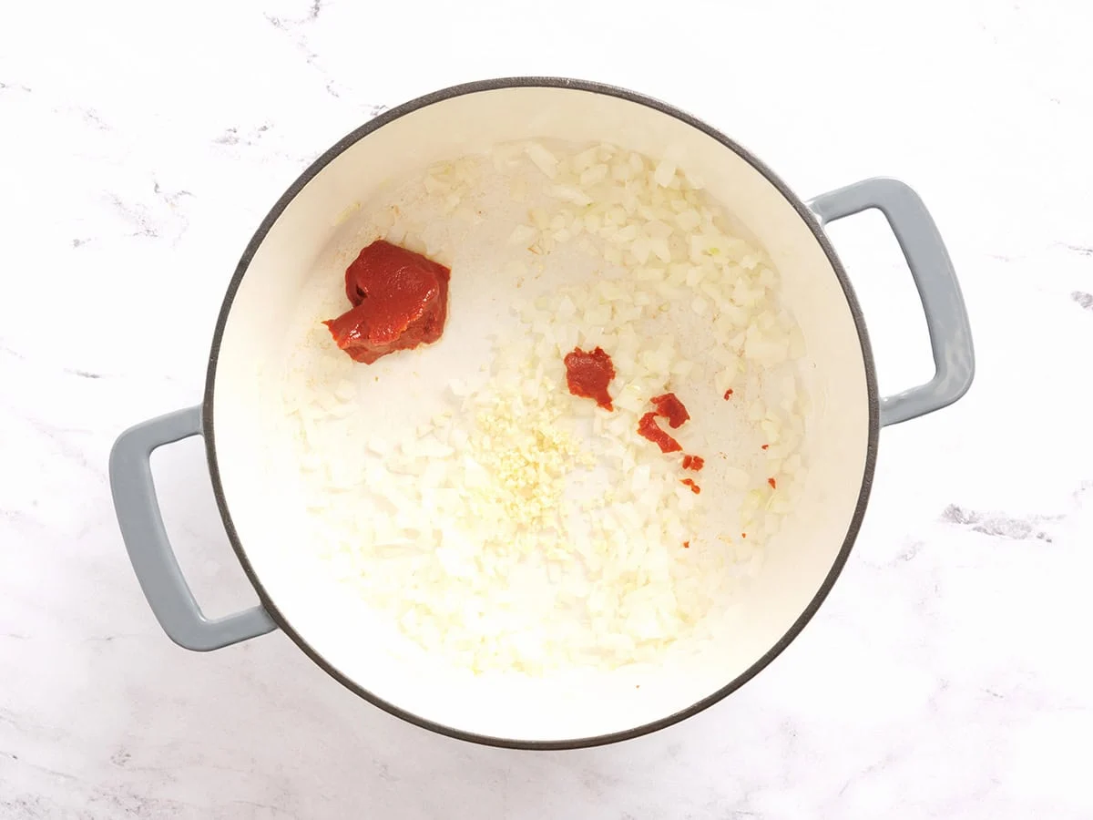 Pâte de tomate et ail émincé ajoutés à l'oignon sauté dans une casserole.
