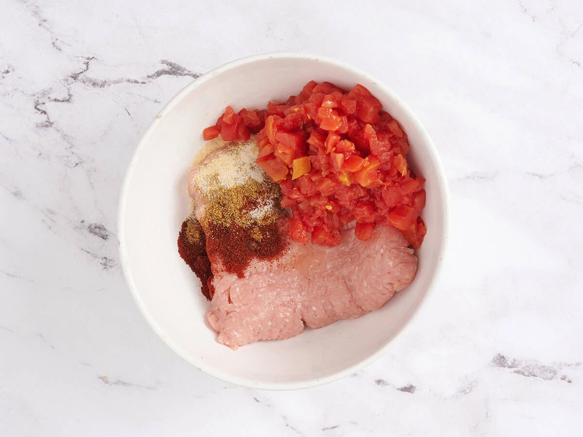 Épices, tomates en dés et dinde hachée dans un bol à mélanger.