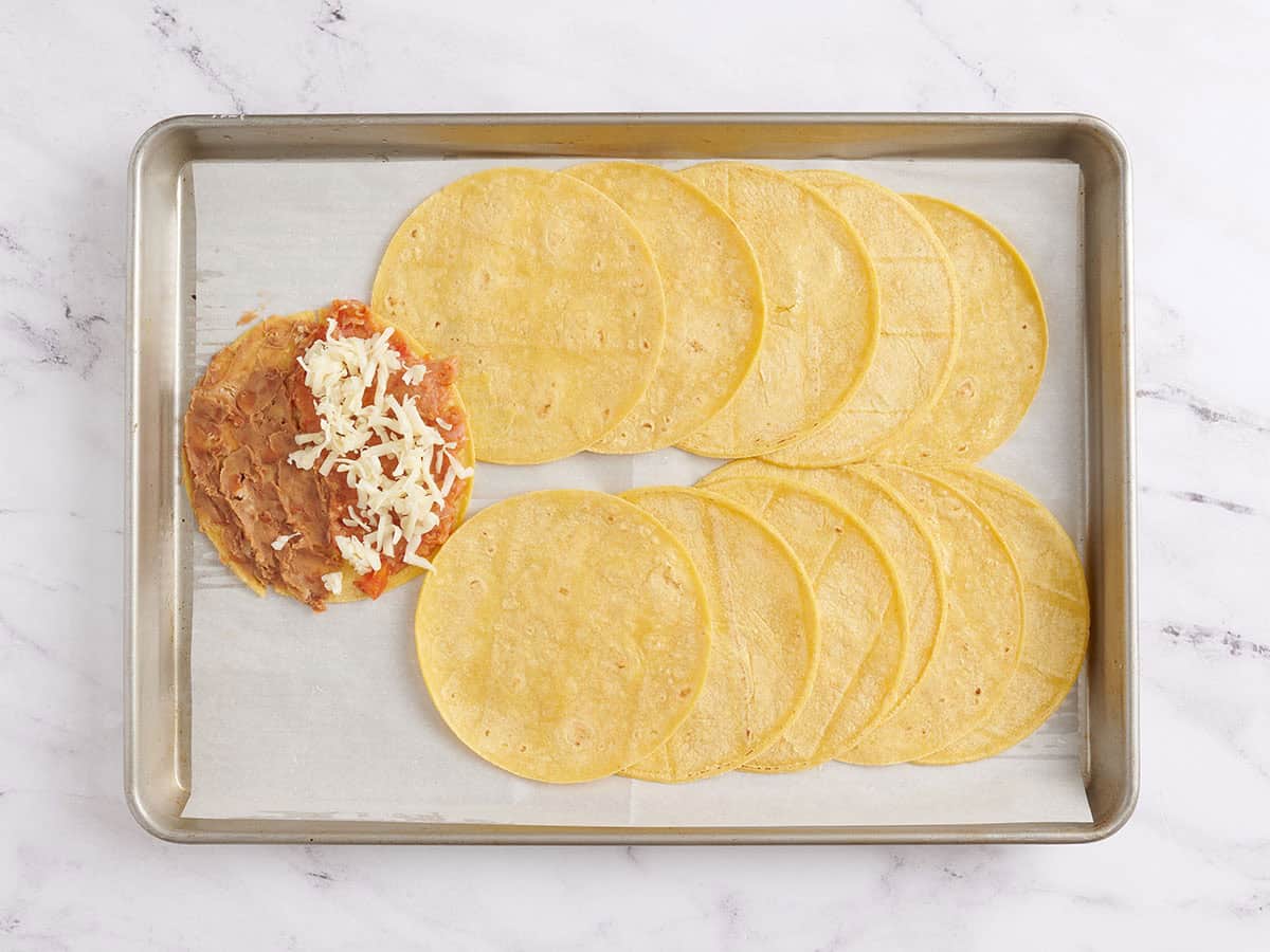 Une tortilla avec de la dinde et des haricots frits garnie de fromage râpé avant la cuisson.