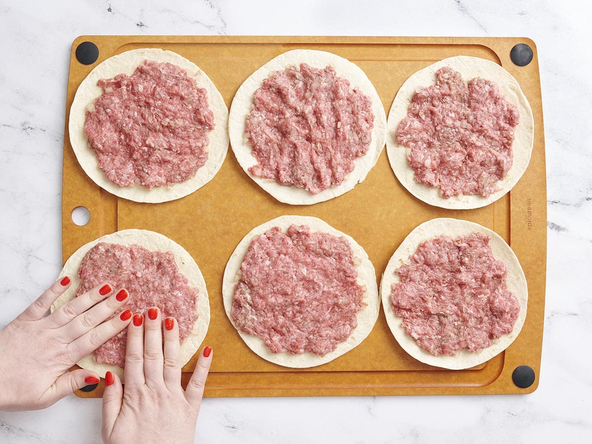 Mains pressant le bœuf haché dans des tortillas à la farine.