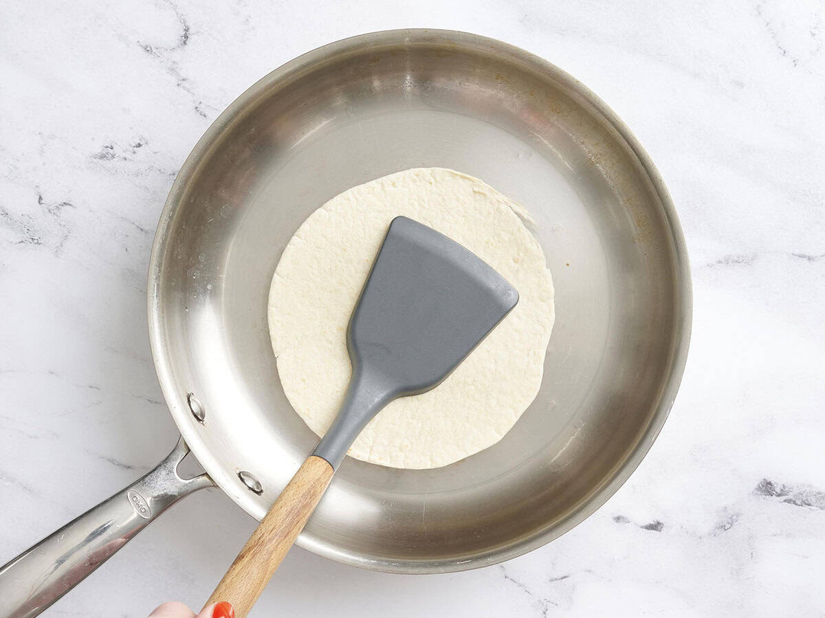 Une spatule pressant une tortilla dans une poêle.