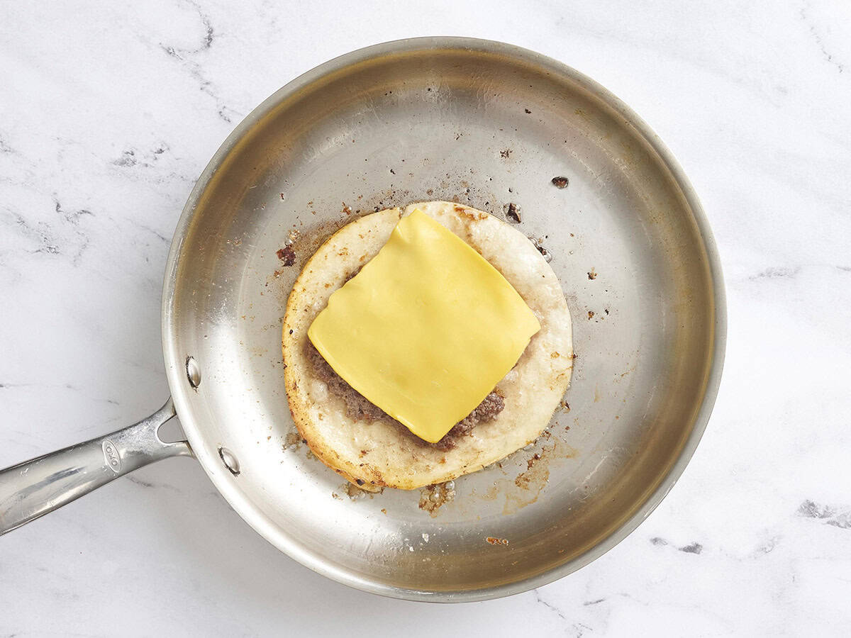 Un taco smash burger dans une poêle surmonté d'une tranche de fromage américain.