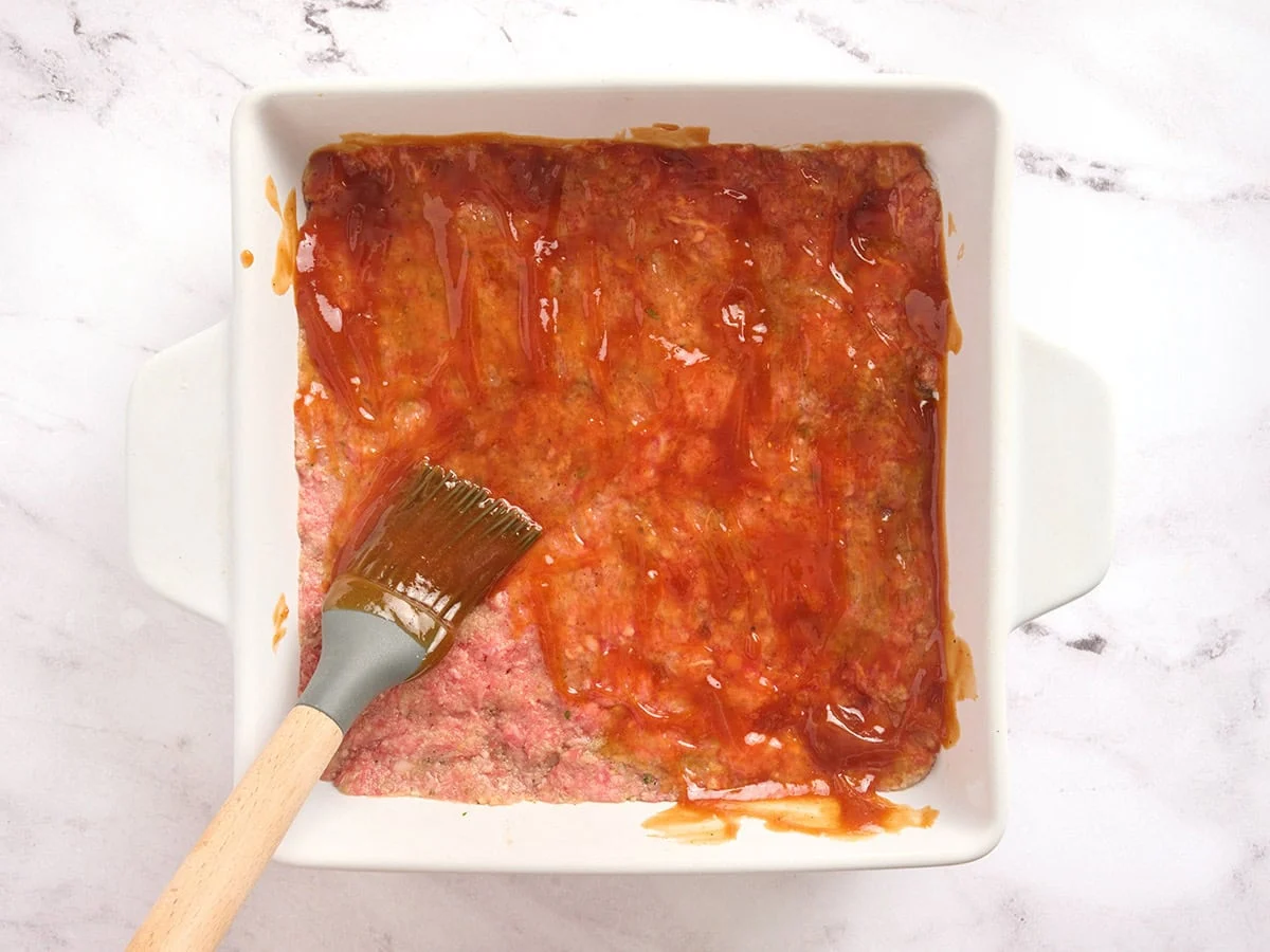 Un glaçage au ketchup étalé sur un pain de viande dans une cocotte.